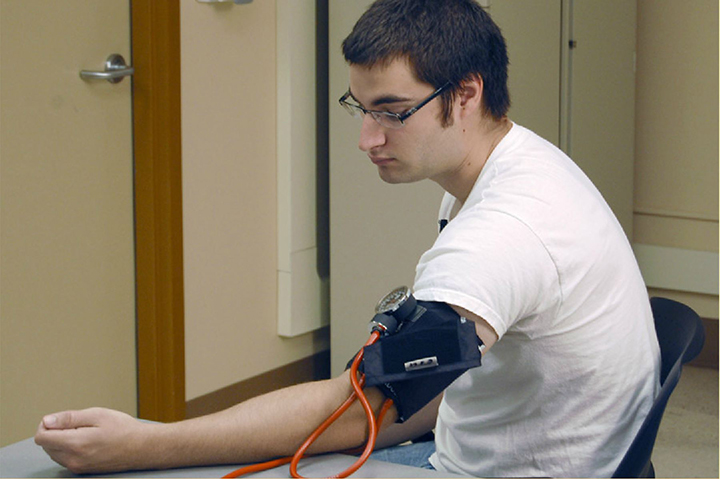 patient sitting with blood pressure cuff on, looking downward and pale